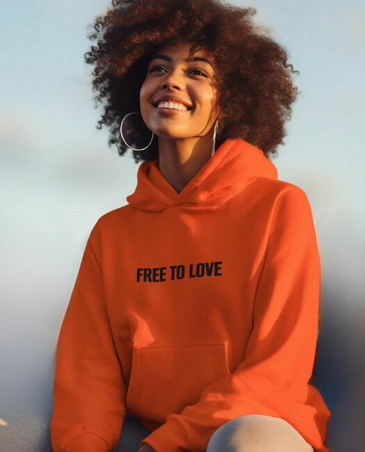 Young smily woman wearing our 100% organic coton "free to love" orange hoodie