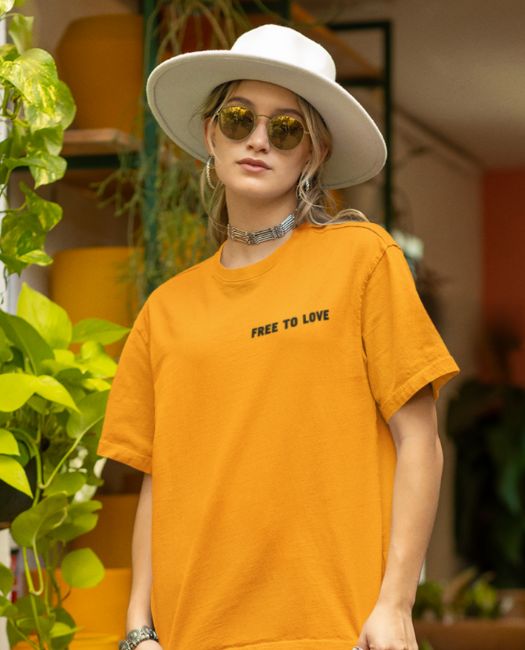 A young woman with a hat and sunglasses, wearing our gold "free to love" t-shirt